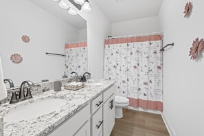 Ein Badezimmer mit zwei Waschbecken, einem Spiegel und einer Duschvorhang mit floralem und Schmetterlingsmuster.