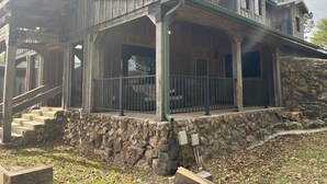 Une maison rustique en bois, avec des fondations en pierre, un porche doté d’une rambarde en métal et un escalier menant à l’étage supérieur.