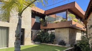 A modern house with a stone facade, a wooden deck, and a well-maintained lawn. - Duas Quintas-areal T1 Varanda (Nespereira GMR)