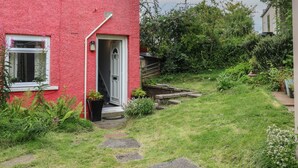 Ein rotes Haus mit einer weißen Tür, ein kleiner Garten mit einem Kiesweg und einem Holzzaun.