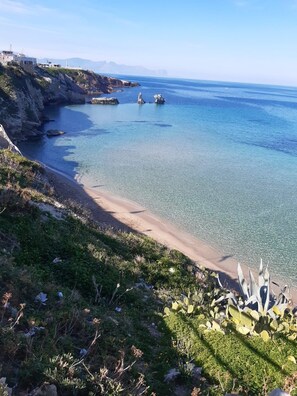 A coastal landscape with a clear beach, rocky cliffs, and sparse vegetation. - Le Antiche Alcove - Charming detached house near the sea (Terrasini)