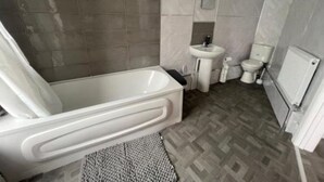 Een moderne badkamer met een bad, wastafel, toilet en een handdoekradiator.