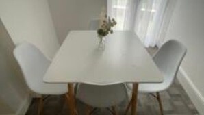 Een eetruimte met een witte tafel en vier witte stoelen.