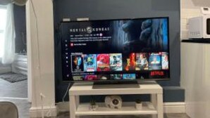 Een flatscreen televisie bevestigd aan een witte standaard in een kamer met een donkerblauwe accentmuur.