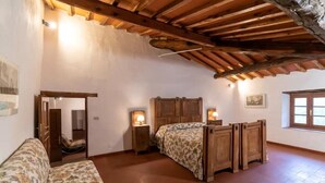 Ein Schlafzimmer mit einem Holzbett, einer Holzbank, einem kleinen Nachttisch mit Lampe, einem floralen Sofa und einem Fenster mit Blick.