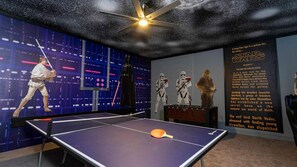 Una habitación con mesa de ping-pong, recuerdos de Star Wars y un ventilador de techo.