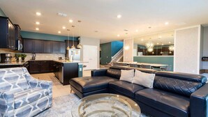 A modern living room with a sectional sofa, a coffee table, and a kitchen area with dark cabinets and a central island. - Luxury Retreat: Windsor Island Villa with Private Pool and Game Room (Davenport)