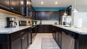 A modern kitchen with dark cabinetry, a granite countertop, stainless steel appliances, and a teal accent wall. - Luxury Retreat: Windsor Island Villa with Private Pool and Game Room (Davenport)