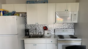 A compact kitchen with white cabinets, a microwave, a stove, and a sink. - Beachfront Condo in Fort Myers Beach (Fort Myers Beach)