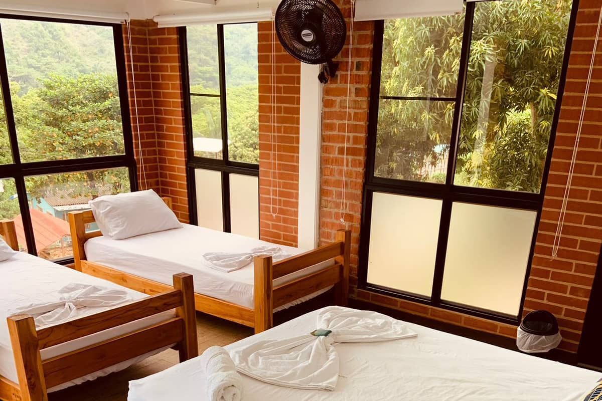 Una habitación de hotel con dos camas de madera, un ventanal grande y un ventilador.