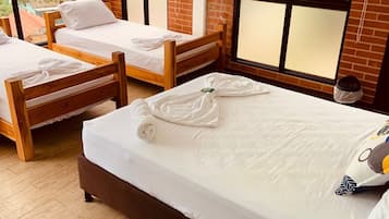 Una habitación de hotel con dos camas de madera, un ventanal grande y un ventilador.
