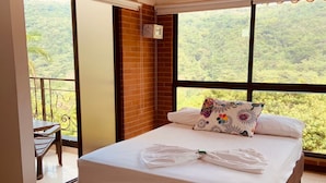 A bedroom with a large bed, a view of the outdoors, and a balcony with a table and chairs.