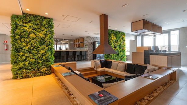 A modern interior with a long wooden reception desk, a seating area with sofas, and a green vertical garden wall.