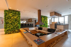 Un interior modern amb una llarga taula de recepció de fusta, una zona d'estar amb sofàs i una paret vertical amb jardí verd.