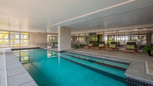 An indoor swimming pool with clear blue water, surrounded by lounge chairs and potted plants.