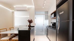 A modern kitchen with a black refrigerator, a dining table with chairs, and a small plant on the island.