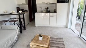 A modern kitchen with white cabinets, a dining area with a sofa and stools, and a large sliding glass door leading to an outdoor area.