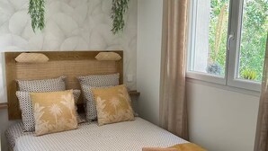 A neatly made bed with patterned pillows, a wooden headboard, and a window with curtains.