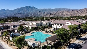 A residential area with a swimming pool surrounded by houses with red-tiled roofs, set against a mountainous backdrop. - Gated PGA West 2023 New Build (EV Charger) (La Quinta)