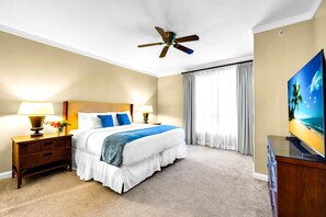 Ein Hotelzimmer mit einem Bett, zwei Nachttischen mit Lampen, einem Deckenventilator, einem großen Fenster mit Vorhängen und einem Fernseher auf einer Holzeinrichtung.