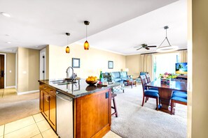 Eine moderne Küche mit Kochinsel, ein Essbereich mit blauen Stühlen, ein Wohnzimmer mit Sofa und ein Deckenventilator.