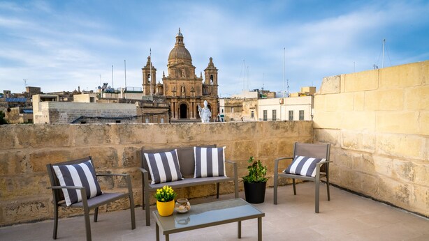 A rooftop terrace with a seating area, a table, and a potted plant.