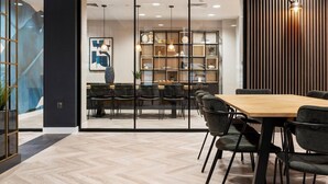 Une salle de réunion moderne, dotée d’une table en bois et de chaises noires, d’une cloison en verre avec des étagères et d’un panneau mural décoratif.