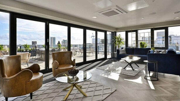 Un intérieur moderne avec de grandes fenêtres, une table basse en verre, des fauteuils en cuir et une vue sur le paysage urbain.