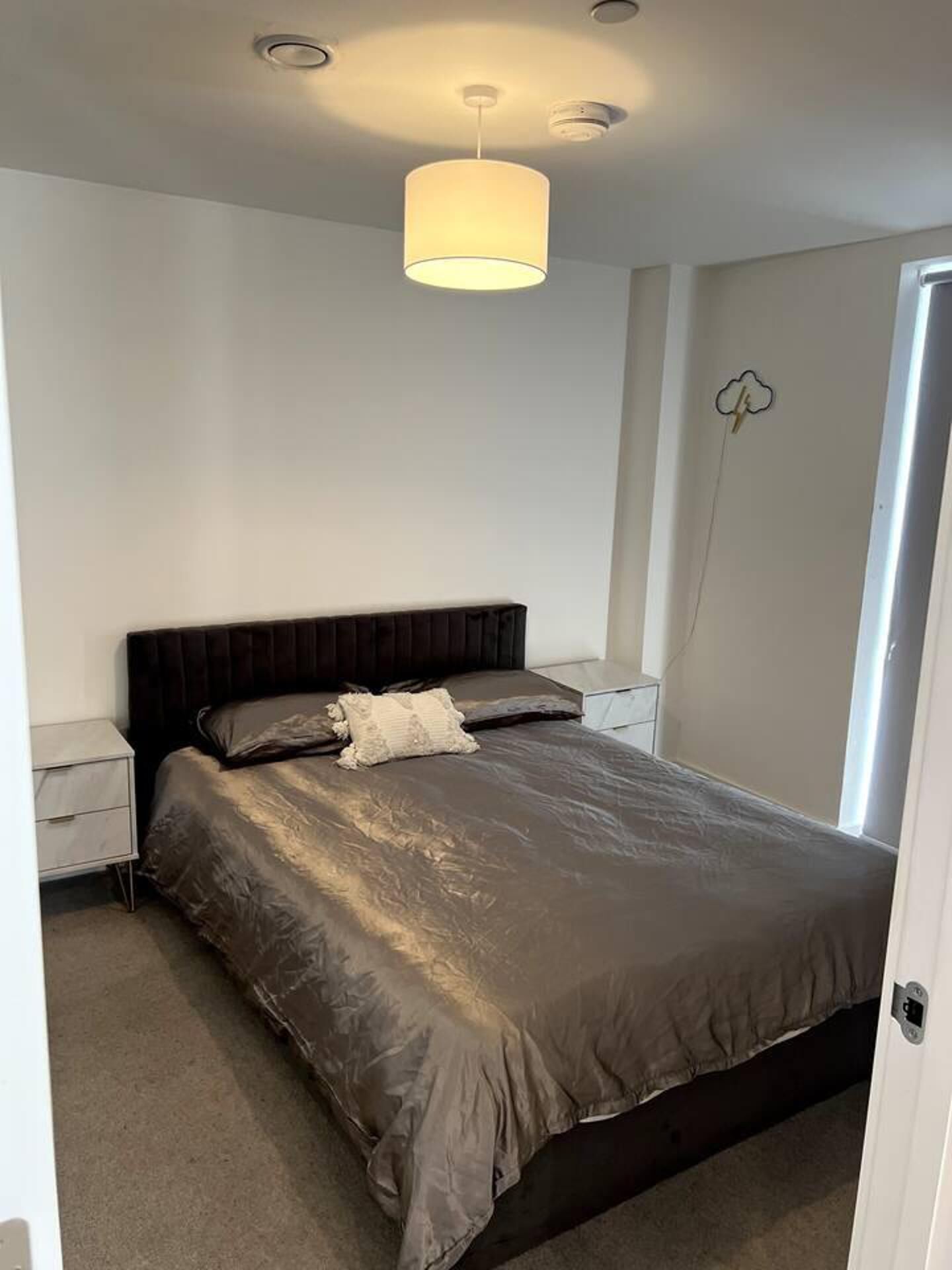Un dormitorio moderno con una cama grande, una mesita de noche, una lámpara de pared y un enchufe.