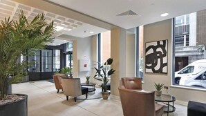 Un hall d’entrée moderne, doté d’espaces de détente, d’une grande œuvre d’art abstraite accrochée au mur et offrant une vue sur la rue.