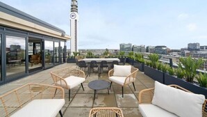 Une terrasse sur le toit, aménagée avec des meubles en osier, dotée d’une structure vitrée et offrant une vue sur la ville.