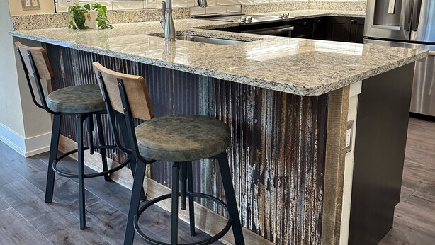 A modern kitchen with dark wood cabinets, a granite countertop, stainless steel appliances, and a bar area with stools. - Luxury Dillon Ski Condo – 2 Master Suites, Heated Garage + Near 7 Ski Resorts (Dillon)