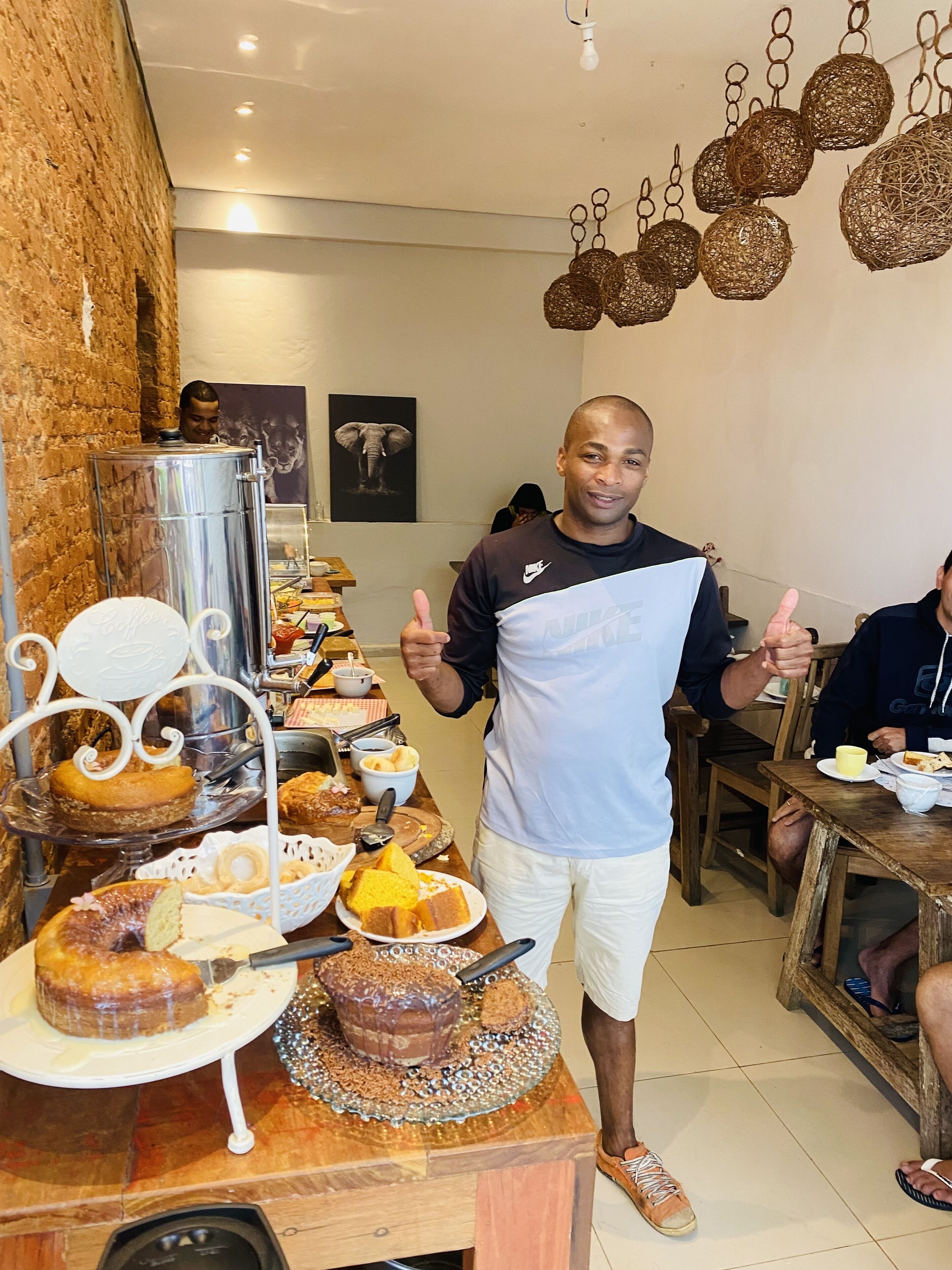 Uma pessoa em pé em um quarto com uma mesa de buffet repleta de diversos pães e doces.