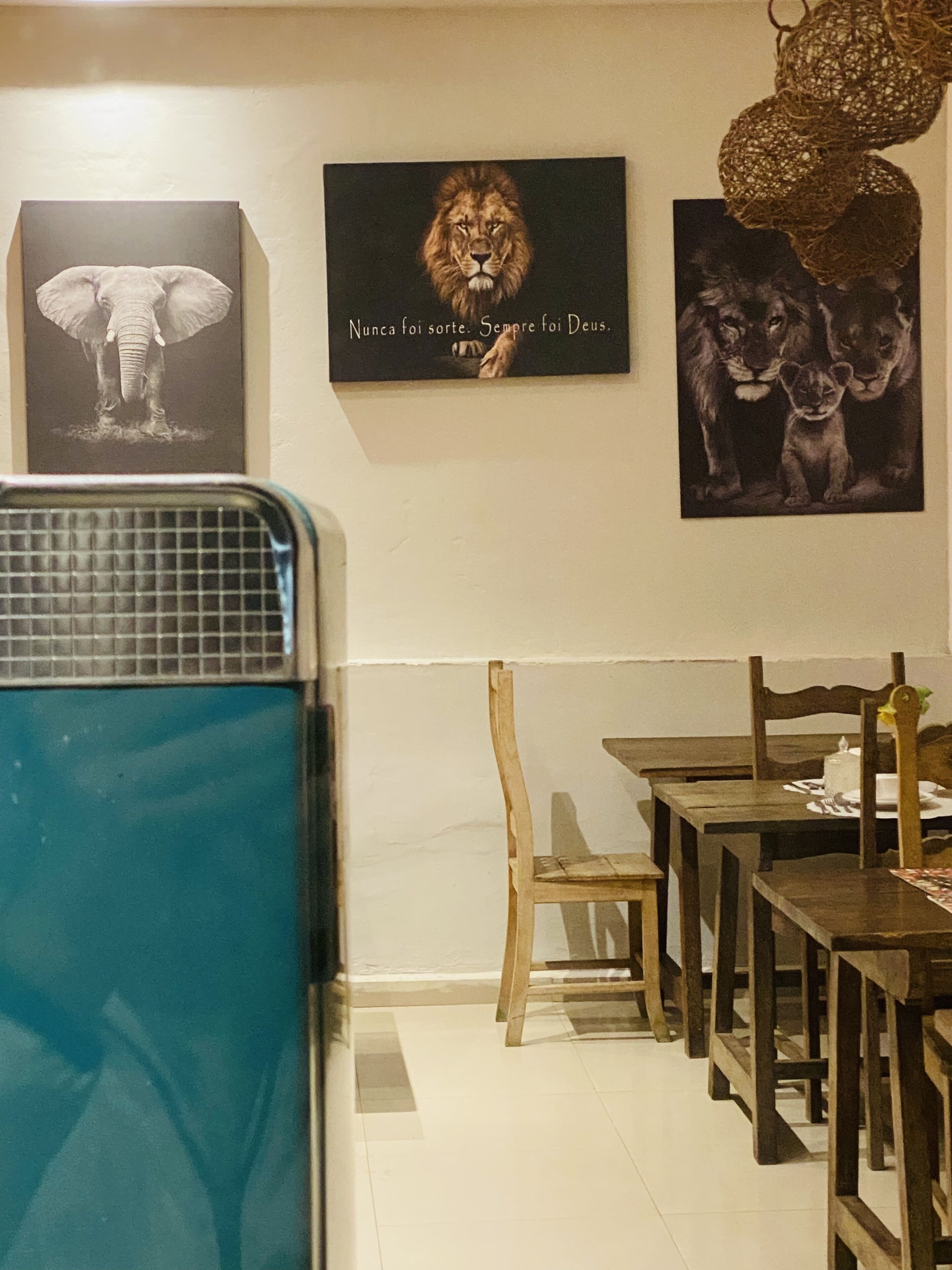 A dining area with wooden tables and chairs, a blue appliance, and three framed animal portraits on the wall.