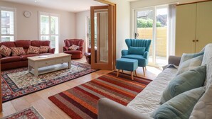 A spacious living room with a red leather sofa, a blue armchair, and a white sofa. There is a wooden coffee table and a patterned rug on the floor. - Wellington Cottage (Ely)