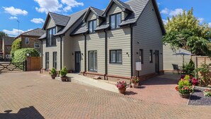 A two-story residential building with a symmetrical facade, a covered patio area with outdoor seating, and a brick driveway. - Wellington Cottage (Ely)