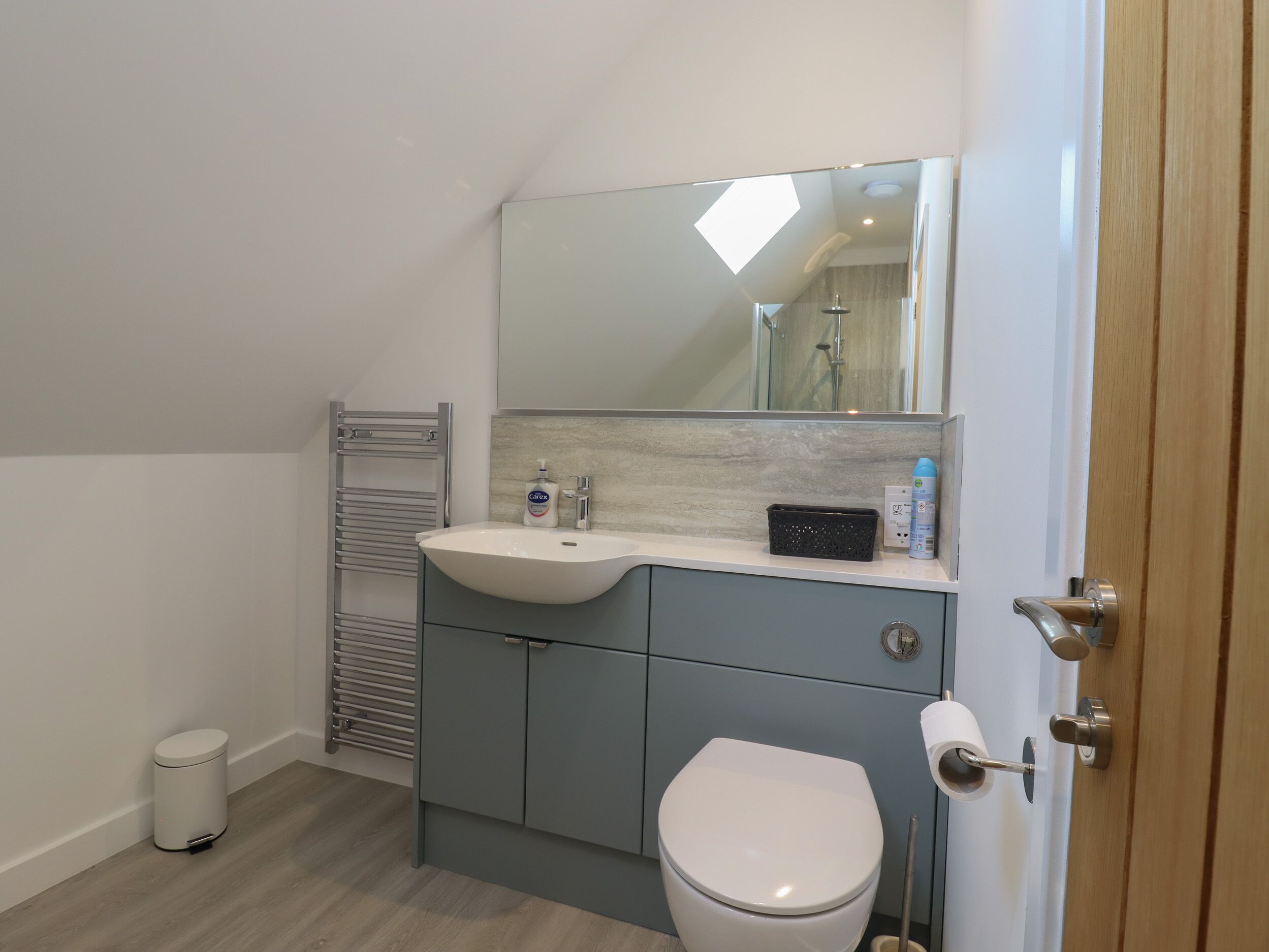 A modern bathroom with a white sink, a mirror, a towel rack, a toilet, and a trash bin.