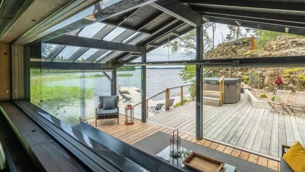 Een modern interieur met grote ramen met uitzicht op een houten terras en een waterpartij.
