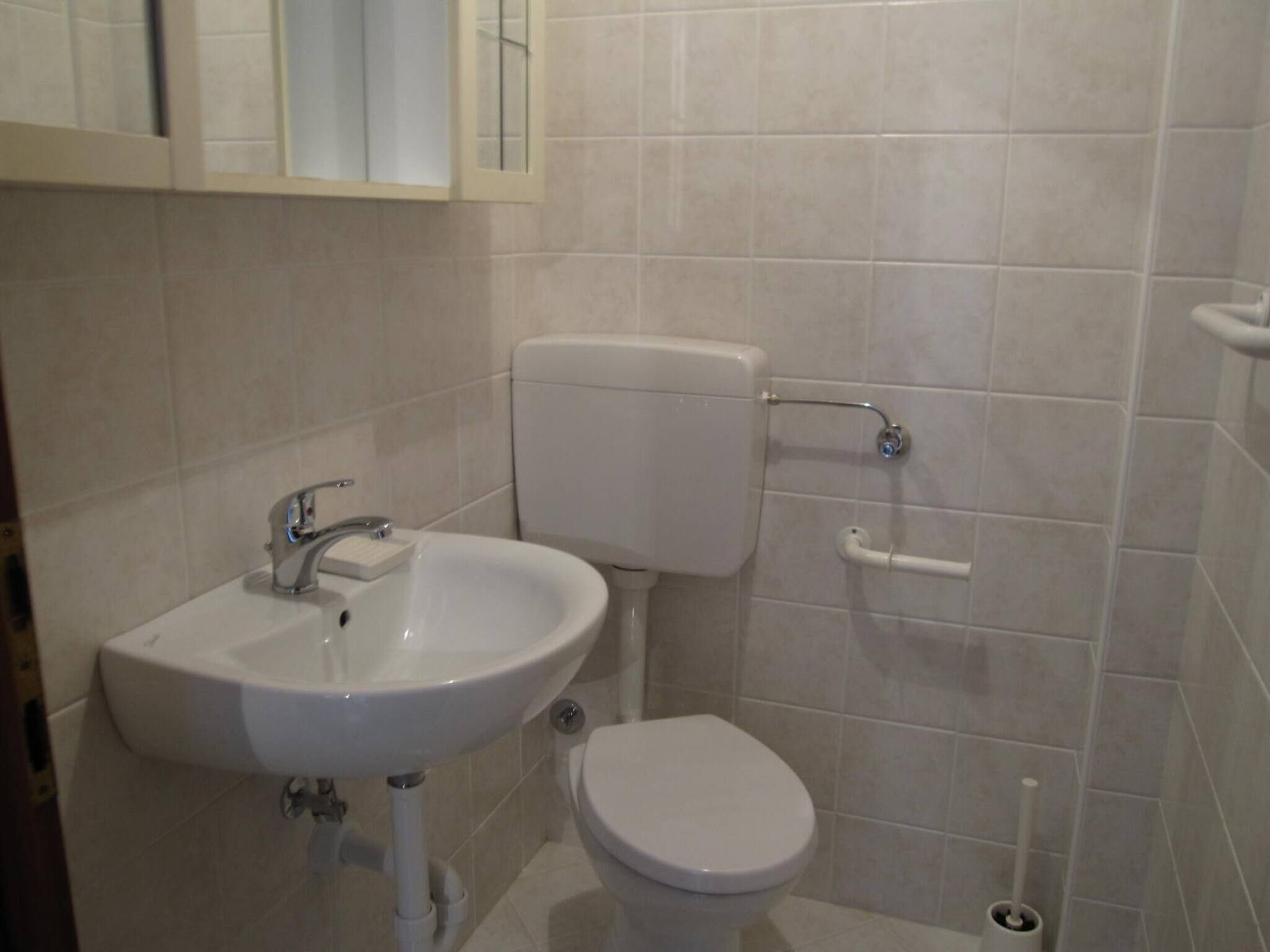 Et lille badeværelse med en hvid vask, toilet og gelænder på væggen.
