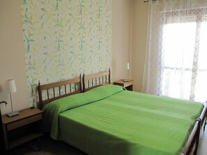 A bedroom with a bed, a nightstand, a lamp, and a window with a curtain. - Amazing Apartment With Seaview Terrace (Grado)