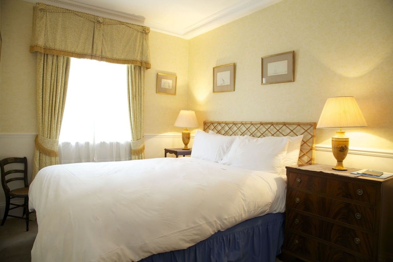 A hotel room with a bed, two bedside tables, a chair, and a window with curtains.