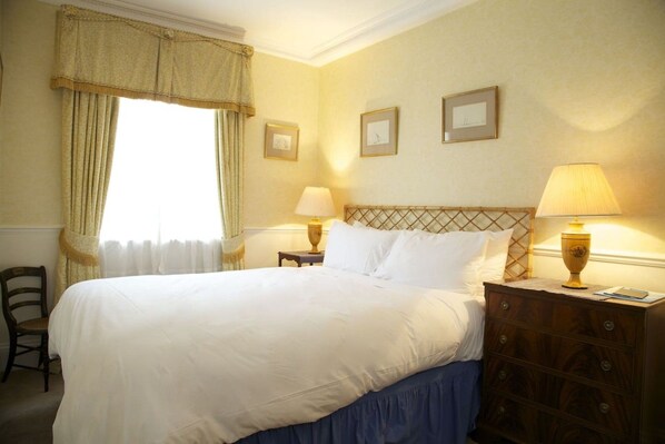 A hotel room with a bed, two bedside tables, a chair, and a window with curtains.