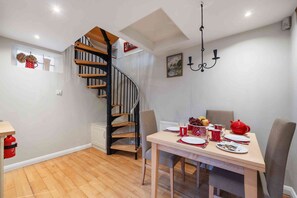 Un coin repas avec une table en bois dressée pour quatre personnes, un escalier en colimaçon et un lustre.