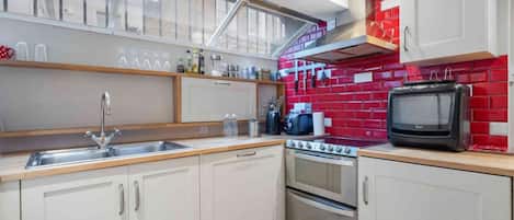 A modern kitchen with white cabinets, a stainless steel sink, a stove, and a red-tiled backsplash.