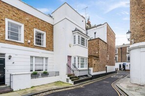A narrow street with traditional brick houses, a white building with a bay window, and a clear sky.