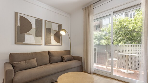 A modern living room with a sofa, a round wooden table, and two abstract wall art pieces. - SAGRADA FAMILIA (Barcelona)