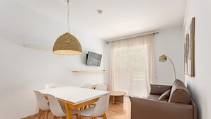 A modern living room with a dining area, featuring a white table, chairs, a sofa, and a TV on the wall. - SAGRADA FAMILIA (Barcelona)