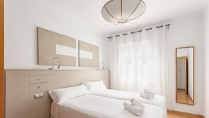 A hotel room with two beds, a large mirror, a ceiling light fixture, and a window with sheer curtains. - SAGRADA FAMILIA (Barcelona)