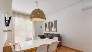 A modern dining area with a white table, four chairs, a woven pendant light, a sofa, and abstract wall art. - SAGRADA FAMILIA (Barcelona)