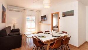 Ein modernes Wohnzimmer mit Essbereich, ausgestattet mit einer Couch, einem Esstisch, Stühlen und einem Fernseher.